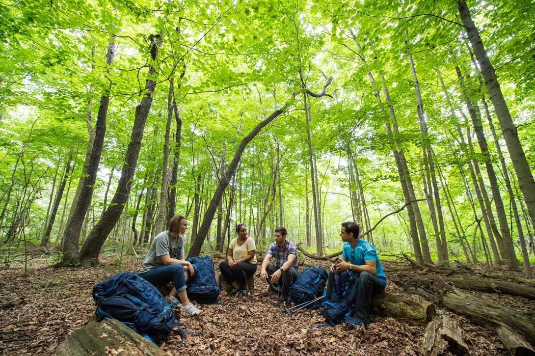 Photograph of four people sitting in a forest with hiking gear.