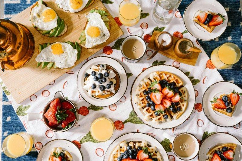Photograph of a table with breakfast foods and drinks, including pancakes, waffles, orange juice, and coffee.